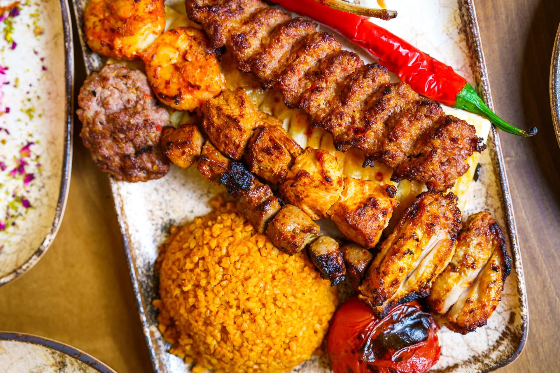 Nahaufnahme einer Grillplatte mit Spießen, Reis und Paprika