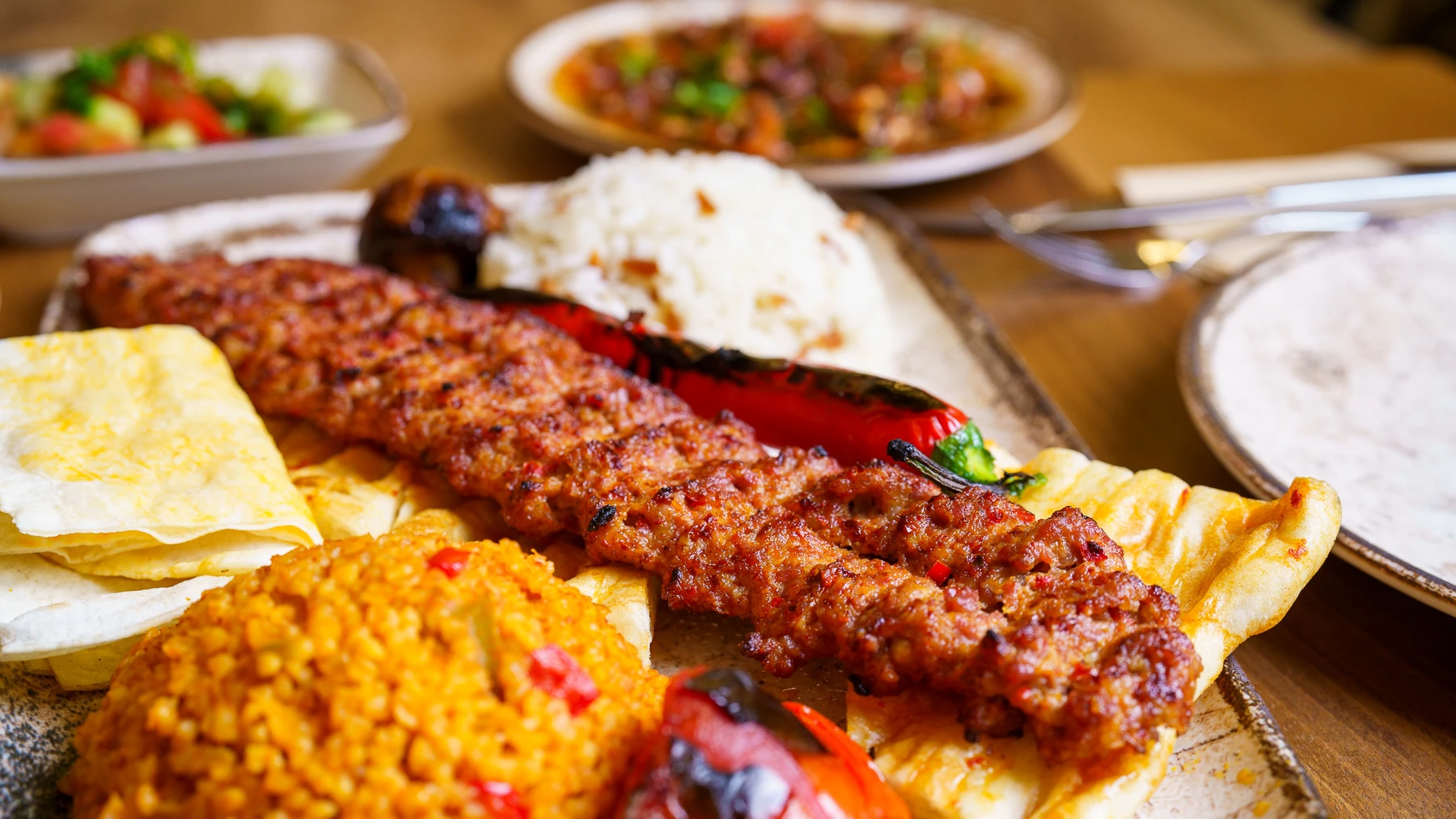 Adana skewers with bulgur and grilled vegetables on a ceramic plate