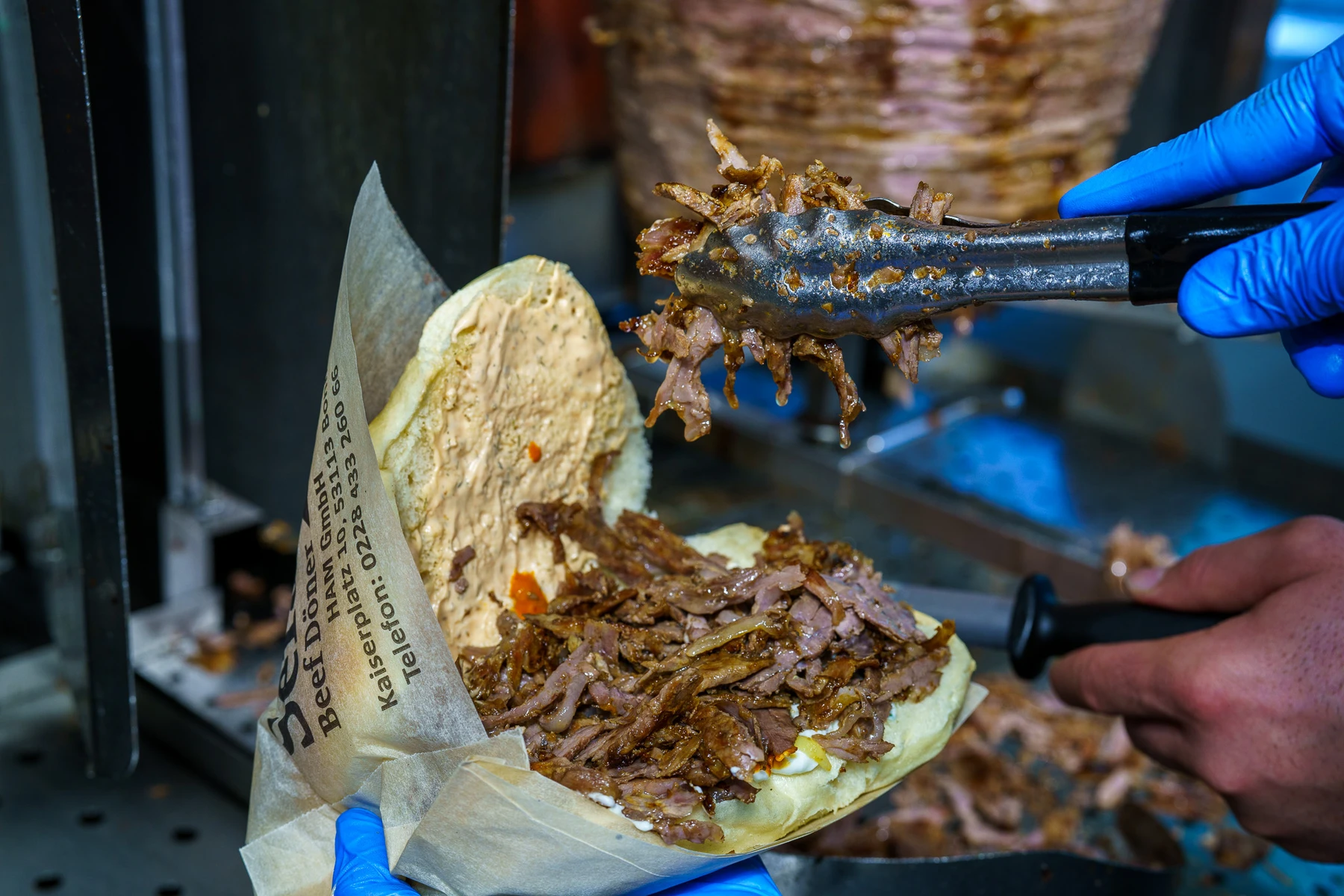 A member of staff filling bread with freshly carved döner meat beside the spit